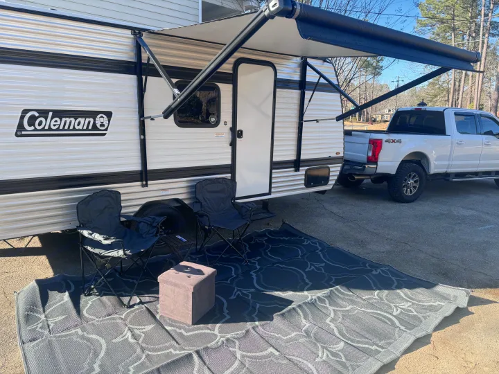 Coleman travel trailer RV rental with extended awning, camping chairs, and an outdoor rug setup.. Keystone Coleman 17B 2025