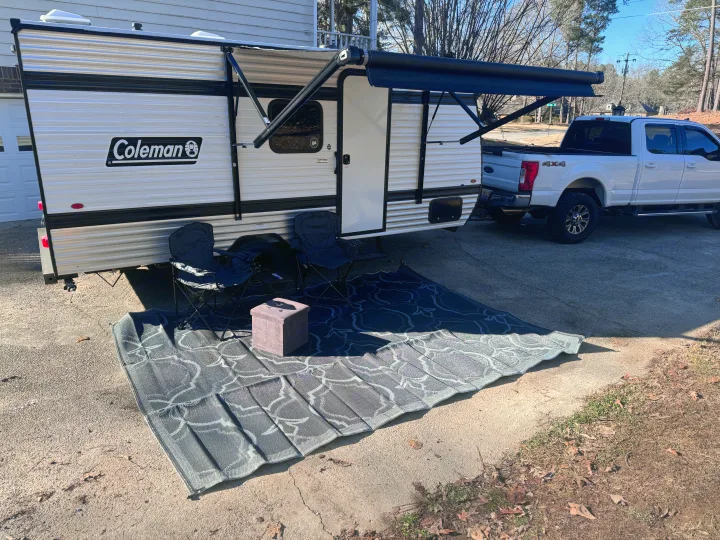 Coleman travel trailer rv rental setup: extended awning, outdoor rug, and chairs for sunny relaxation.. Keystone Coleman 17B 2025