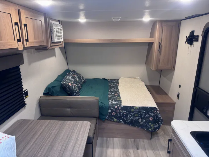 Cozy RV rental interior with a comfortable bed, dinette, overhead cabinets, and a compact kitchenette.. Keystone Coleman 17B 2025