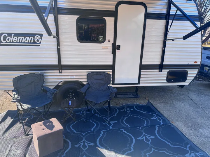 Coleman RV rental: White travel trailer with an extended awning, outdoor rug, and two camping chairs create a cozy setup.. Keystone Coleman 17B 2025