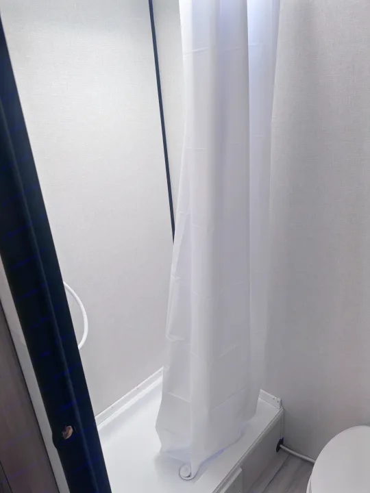 A compact RV rental shower stall with a white curtain and light grey textured walls.. Keystone Coleman 17B 2025