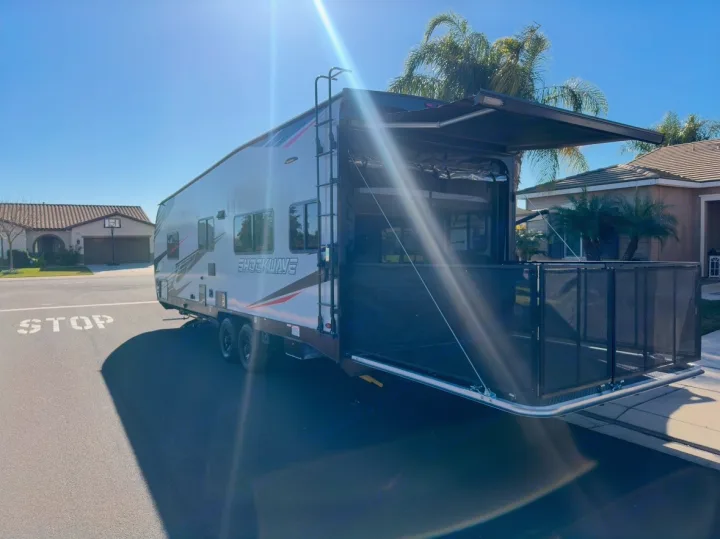 Toy hauler RV rental: Rear ramp lowered, creating a patio with safety rails and awning, parked on a sunny street.. Forest River Shockwave 2021