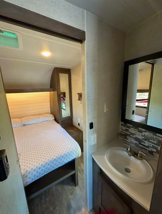 Explore this RV rental's inviting bedroom and practical bathroom, designed for comfortable travel trailer trips.. Forest River Shockwave 2021