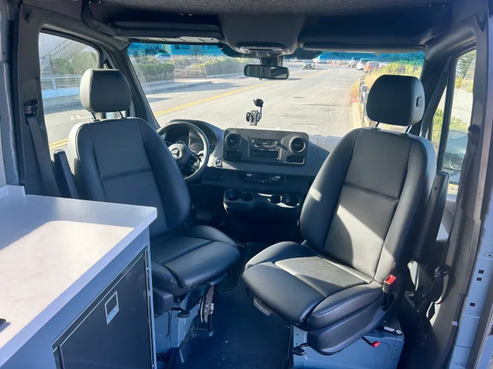 Inside a spacious RV rental camper van, featuring comfy front seats, dashboard, and a clear road ahead.. Mercedes-Benz Sprinter 144 2023