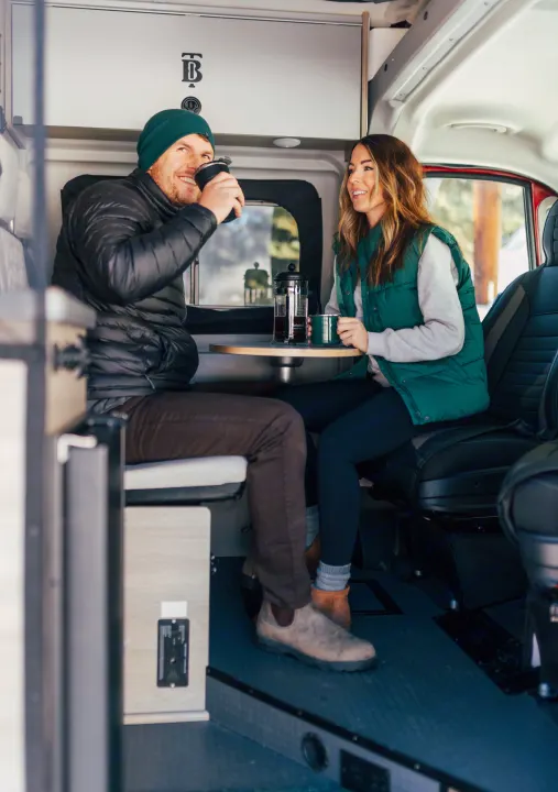 A joyful couple enjoys coffee inside their modern RV rental, perfect for cozy road trips and camping adventures.. Winnebago Solis 2022