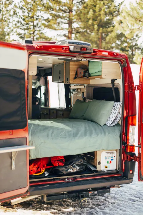This RV rental shows a camper van's open rear doors, revealing a comfy bed, overhead cabinets, and under-bed storage.. Winnebago Solis 2022