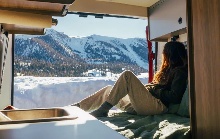 Inside a cozy RV rental, a person enjoys vast snowy mountain views. Ideal for a winter travel adventure.. Winnebago Solis 2022