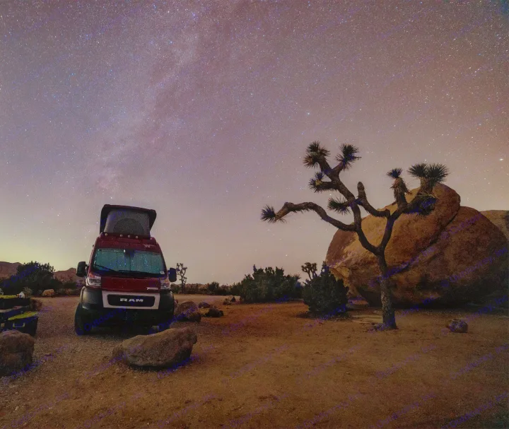 An RV rental rests under a starry night sky, featuring a Joshua tree and desert landscape. Ideal for stargazing trips.. Winnebago Solis 2022