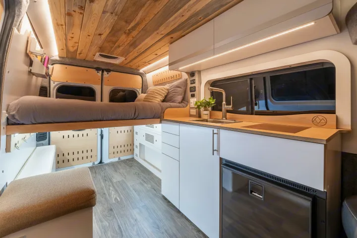 Explore a cozy, well-designed camper van interior, perfect for your next rv rental adventure. Features bed, kitchen, and warm lighting.. Dodge Ram 1500 2024