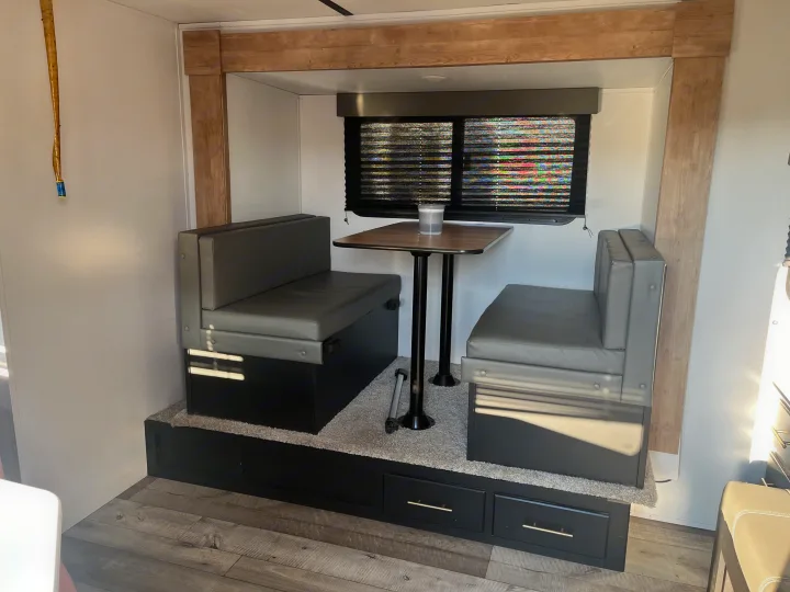 Modern RV rental dinette with gray booth seating, square table, and storage drawers on a carpeted platform.. Keystone RV Springdale 2022