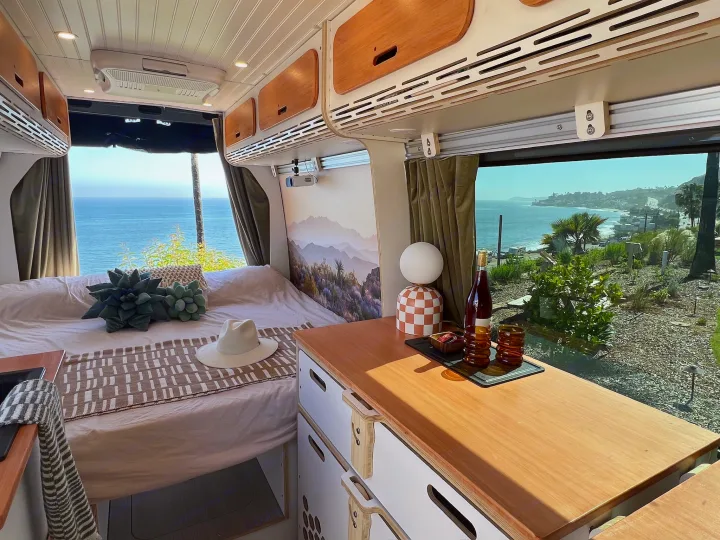 **RV rental** interior with a comfortable bed, modern cabinets, and a counter. Enjoy stunning ocean views from this cozy camper van.. Mercedes-Benz Sprinter 2022