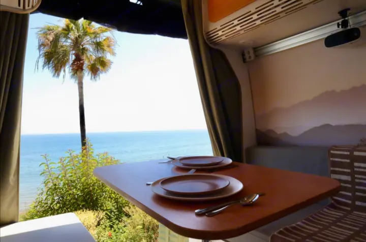 Scenic RV rental dining area overlooking the ocean with a palm tree, set for two. Perfect for a mobile getaway.. Mercedes-Benz Sprinter 2022
