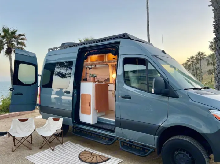 Beachside RV rental: A gray camper van with open doors reveals its cozy interior kitchen & outdoor seating. Ideal for glamping.. Mercedes-Benz Sprinter 2022