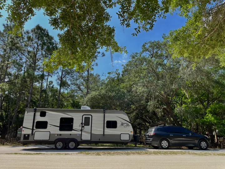 RV rental: A grey travel trailer & SUV are parked in a sunny campsite surrounded by tall pines & oak trees.. Jayco Jay Flight SLX 2021