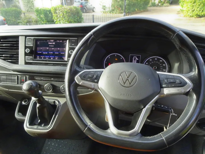RV rental: cockpit view showing a manual gear stick, VW steering wheel with controls, and active infotainment display.. Volkswagen T6.1 Campervan 2021