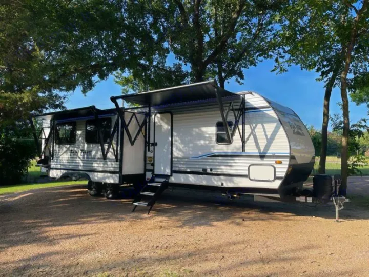This white rv rental travel trailer sits ready at a sunny campsite with awnings out, perfect for outdoor adventures.. Crossroads RV Funtime 333sk 2024