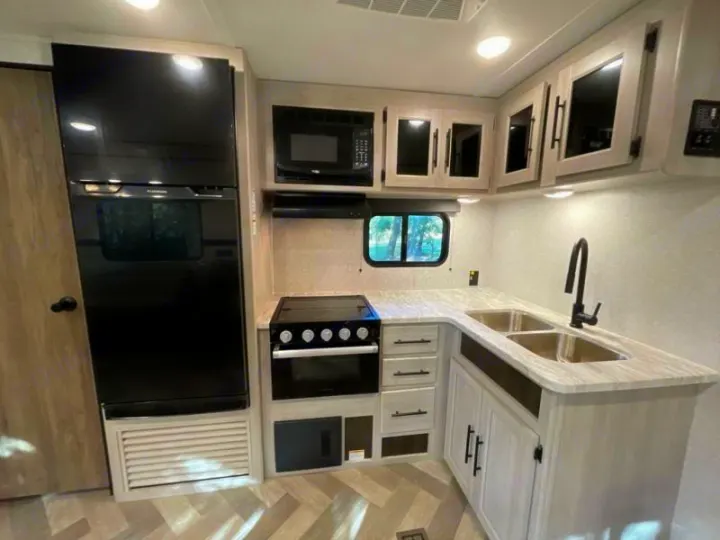 Modern RV rental kitchen featuring a black fridge, stove, microwave, and double sink, with light countertops.. Crossroads RV Funtime 333sk 2024