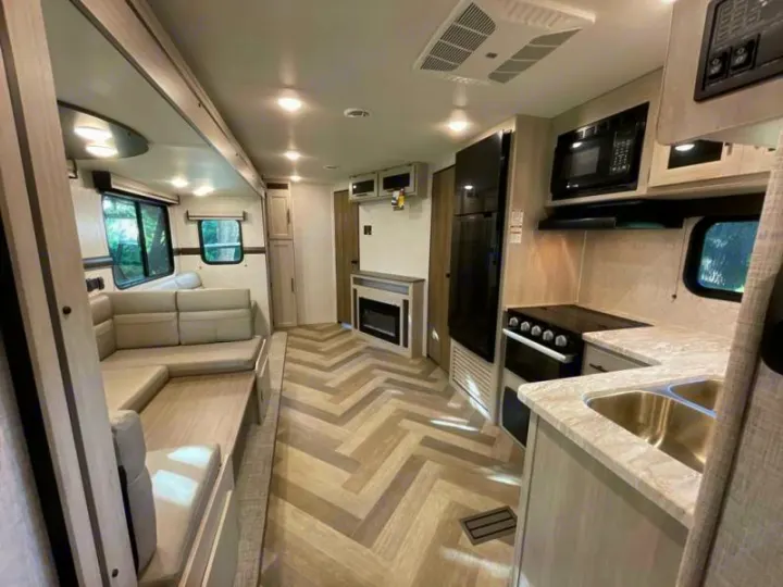 Bright RV rental interior: kitchen with fridge & stove, L-shaped dinette, and fireplace on stylish herringbone floor.. Crossroads RV Funtime 333sk 2024