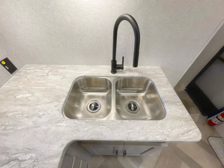 Modern RV rental kitchen: double stainless steel sink, black faucet, and light granite-look counter. Perfect for travel!. Crossroads RV Funtime 333sk 2024