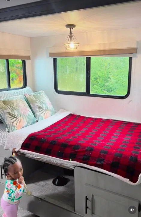Inside a cozy RV rental bedroom: bed with plaid blanket, windows, & toddler playing. Ideal for travel.. Forest River IBEXMBS 2023