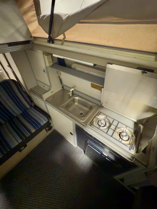 Compact RV rental interior: kitchen with sink, two-burner stove, fridge, and seating area. Features a pop-up roof.. Winnebago Eurovan Camper Eurovan Camper 1999