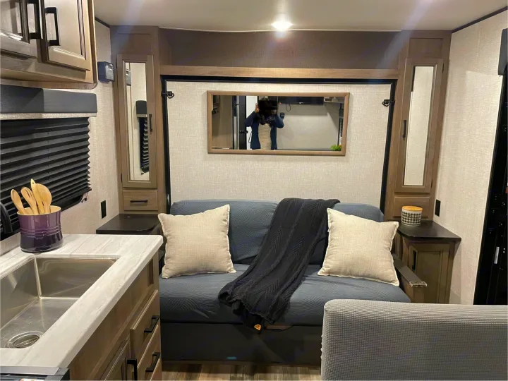 Cozy RV rental interior: A compact living space with a gray sofa, sink, and mirror reflecting a person.. Jayco Autumn Ridge 20MB 2023