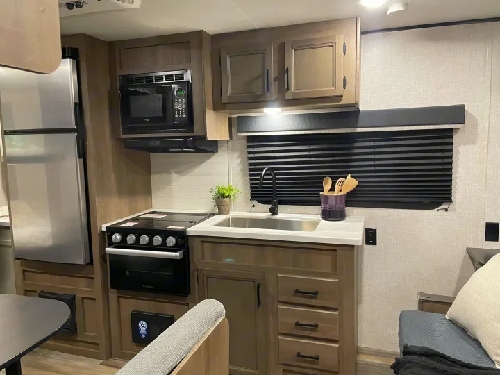 Functional RV rental kitchen with stainless steel fridge, microwave, oven/stove, sink, and ample storage.. Jayco Autumn Ridge 20MB 2023