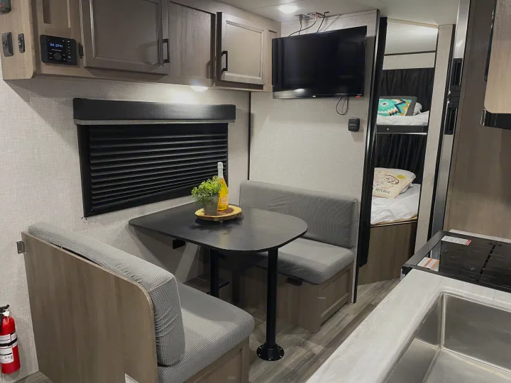 RV rental interior showcasing a practical dinette, overhead storage, compact kitchen, and bunk beds for comfortable living.. Jayco Autumn Ridge 20MB 2023