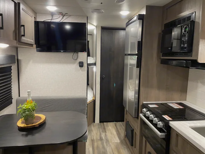 Spacious RV rental interior: equipped kitchen (microwave, stove, fridge), dining booth, TV, and comfy bunk beds.. Jayco Autumn Ridge 20MB 2023