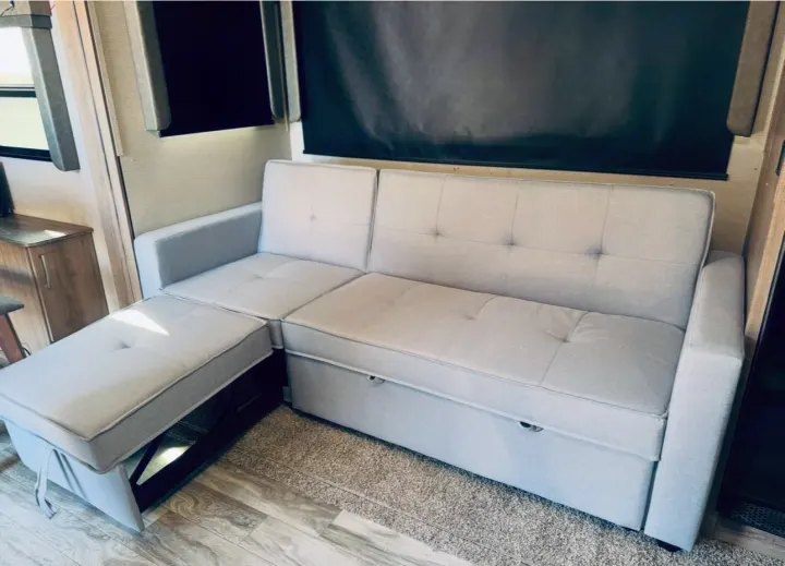 Light gray tufted sectional sofa, with an extending ottoman and hidden storage, offers comfort in this RV rental.. Grand Design Imagine 2022