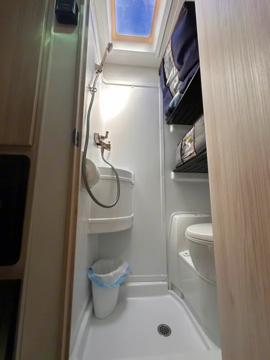 Compact RV rental wet bath with shower, toilet, sink, trash, and storage. Skylight visible.. Winnebago Other 2023
