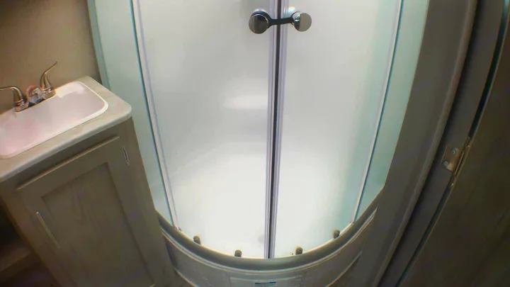A compact RV rental bathroom features a sink, light wood cabinet, and curved frosted glass shower.. Coachmen Catalina 2021