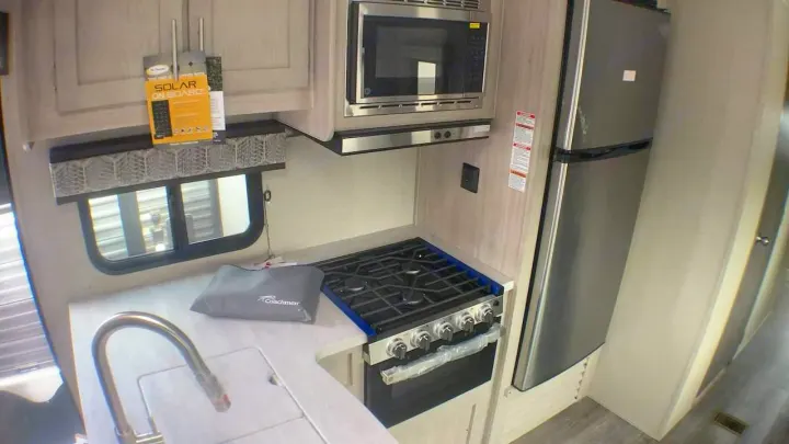 This RV rental features a compact kitchen with a sink, microwave, 4-burner stove, oven, and tall fridge. "Solar On Board" sign visible.. Coachmen Catalina 2021