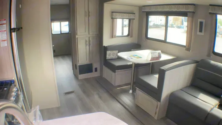 Inside a clean RV rental, showcasing a light wood interior with a dining booth, sofa, and galley kitchen.. Coachmen Catalina 2021