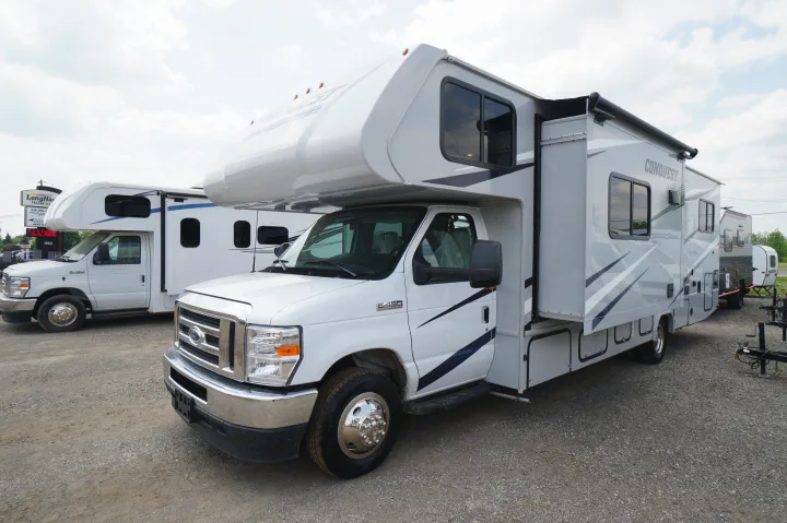 White Ford E-450 Class C RV with a slide-out, parked on a gravel lot at a dealership. Ideal for RV rental or purchase.. Gulf Stream Conquest 2024