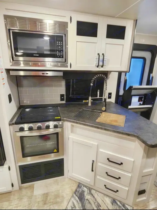 This RV rental features a well-equipped, compact kitchen with stainless steel microwave, oven, range, and sink, set against white cabinetry and dark counters.. Palomino Puma 2024