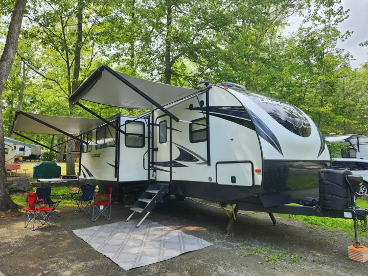 Spacious RV rental set up at a shaded campsite, featuring extended awnings, outdoor seating, and a grill for a relaxing stay.. Prime Time Lacrosse 2019