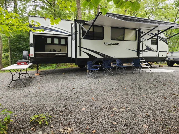 This RV rental is set up on a gravel campsite, featuring an outdoor kitchen, awning, and chairs for a perfect camping trip.. Prime Time Lacrosse 2019