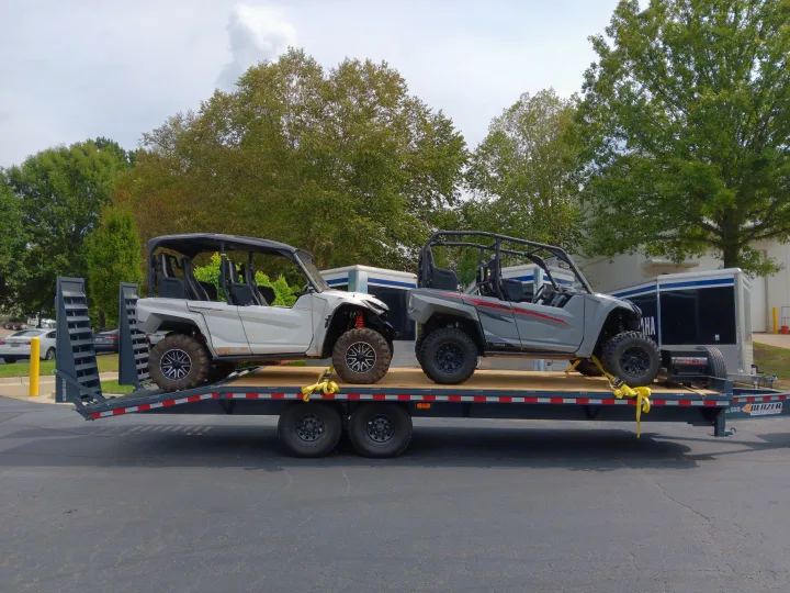 Two Yamaha RMAX side-by-sides are securely loaded on a flatbed trailer, ready for powersports adventures or an RV rental getaway.. Blazer Deck over / Flatbed 2023