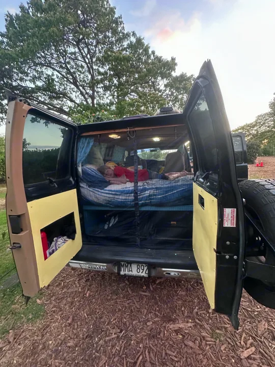 An RV rental camper van with open back doors. A person sleeps on a bed inside, a Hawaii license plate visible.. Dodge 1500 1999