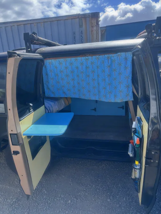 This rv rental features a custom camper van interior: blue palm tree curtain, bed, and a handy fold-down table.. Dodge 1500 1999