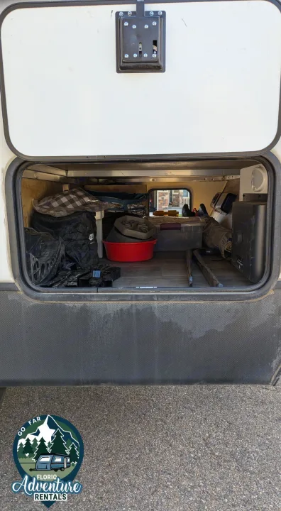 An RV rental's accessible storage compartment, packed with road trip essentials like a red bucket, bags, and tools.. Keystone RV Cougar 2021