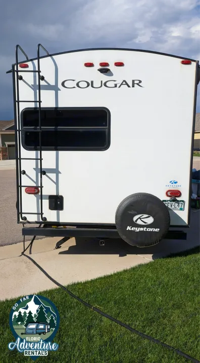 Rear of a white Cougar travel trailer with ladder & spare tire, ready for rv rental adventures.. Keystone RV Cougar 2021
