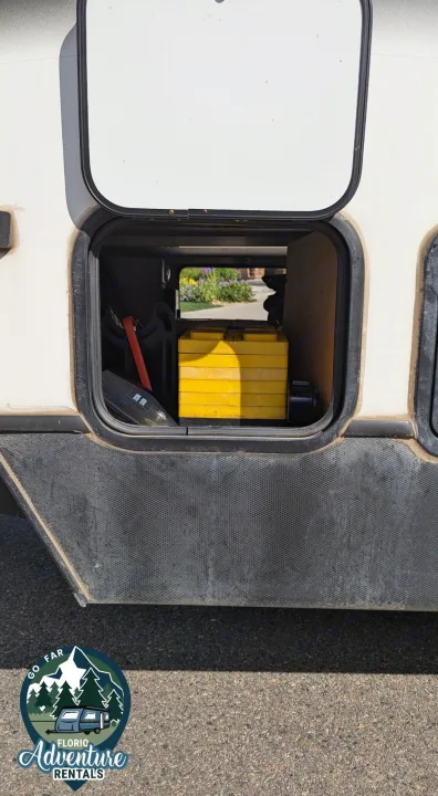 RV rental side storage compartment open, showing yellow leveling blocks & gear for your adventure.. Keystone RV Cougar 2021