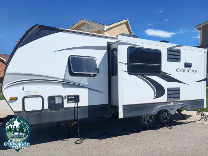 White Cougar RV rental, a travel trailer with extended slide-out, parked on asphalt. Adventure awaits!. Keystone RV Cougar 2021