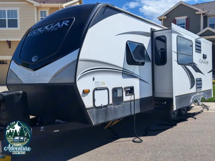 This Cougar travel trailer RV rental, white and black, is parked with its slide-out extended.. Keystone RV Cougar 2021