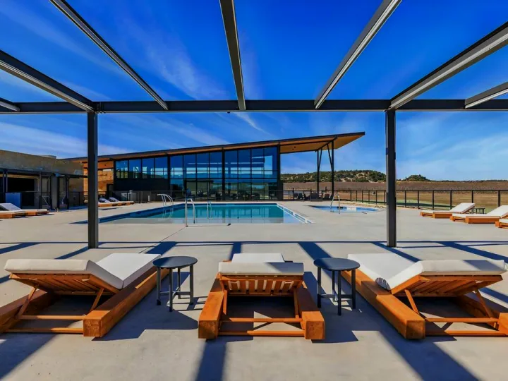 RV rental guests enjoy this modern resort's pool, glassy clubhouse, and outdoor lounge area under blue skies.
