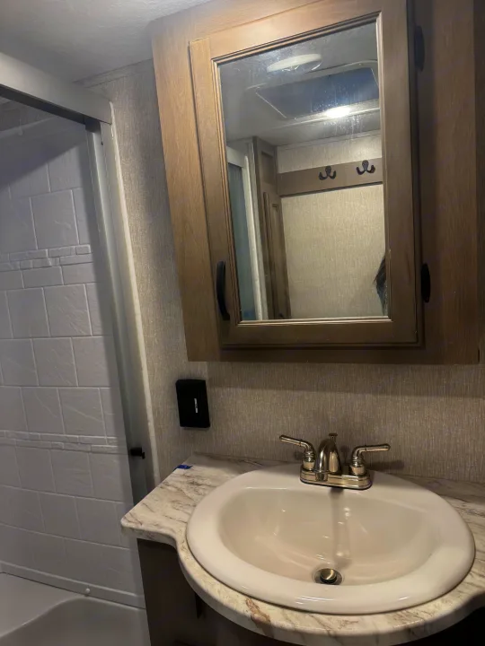RV rental bathroom features a white shower, sink, silver faucet, and wood-framed mirrored vanity cabinet.. Coachmen Chaparral 2022