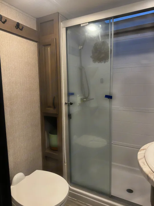 Inside an RV rental: a modern, compact bathroom with a bright shower, toilet, and built-in storage. Practical for travel.. Coachmen Chaparral 2022