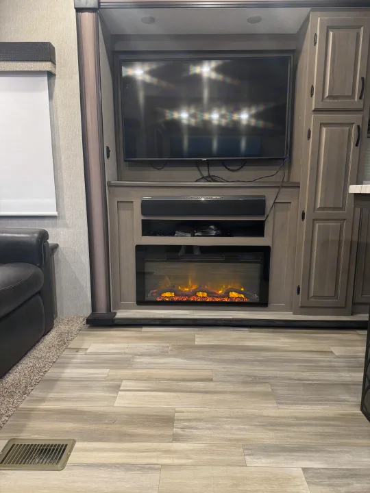 Cozy RV rental living space featuring a wall-mounted TV, soundbar, and electric fireplace, set within light wood cabinetry.. Coachmen Chaparral 2022